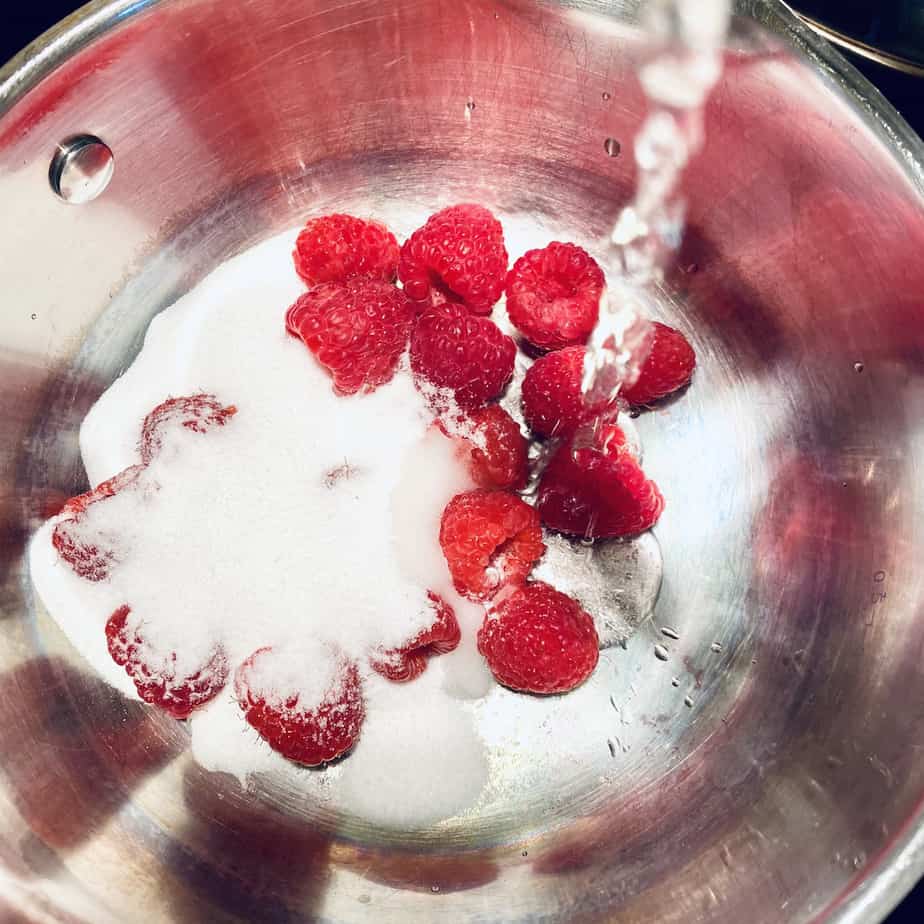 adding sugar and water to raspberries