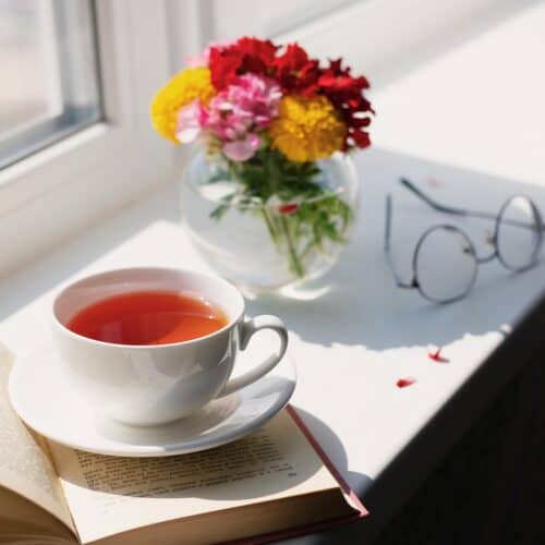improve your life with tea in white cup on table with flowers and book