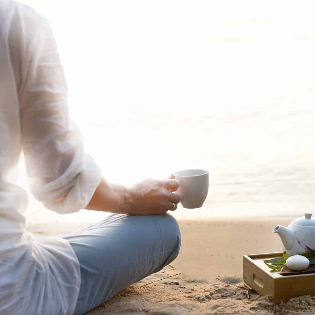 Woman meditating and drinking tea on beach